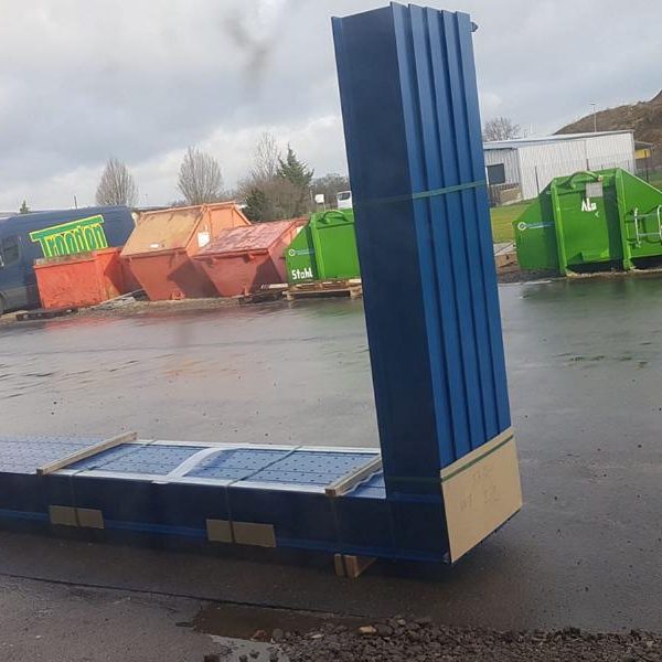 Blauer Container auf einem Grundstück mit mehreren farbigen Abfallcontainern im Hintergrund.