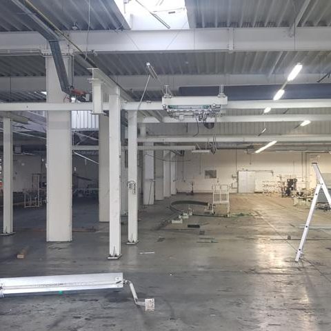 Leerer, heller Lagerraum mit Stromleitungen und sichtbaren Säulen.