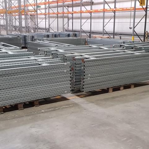 Gestapelte Metallregale in einem Lager mit grauem Boden.