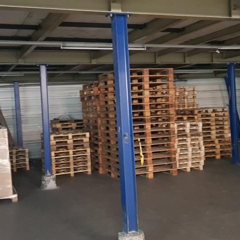 Lager mit mehreren Holzpaletten, gestapelt zwischen blauen Säulen.