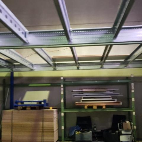 Lagerraum mit Regalen, Holzplatten und einer Stahlkonstruktion über dem Boden.