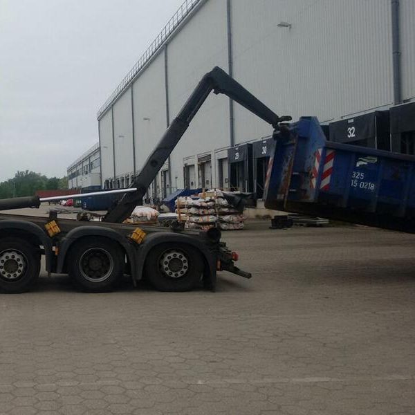 Lkw mit Kran hebt einen blauen Container auf einem Betriebsareal.
