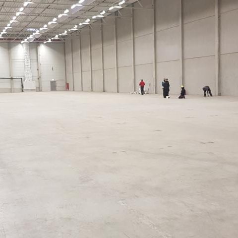 Leere Lagerhalle mit wenigen Personen im Hintergrund, die den Boden reinigen.