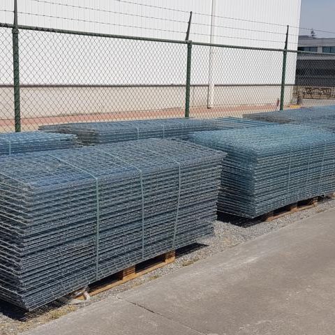 Stapel von verzinktem Drahtgitter auf Paletten, hinter einem Zaun.