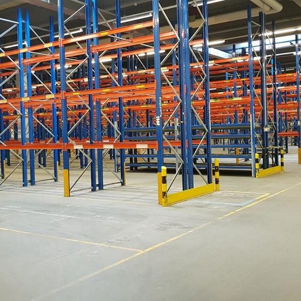 Leere Lagerhalle mit blauen und orangen Regalsystemen.