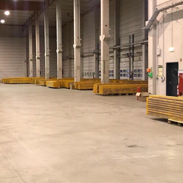 Leerer Lagerraum mit langen, gelben Paletten entlang der Wände.