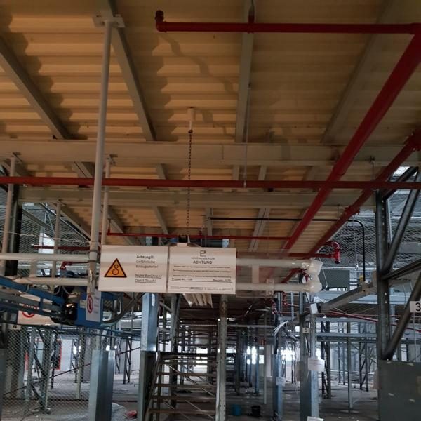 Blick auf eine Baustelle mit rotem und grauem Rohrleitungssystem sowie Warnschildern.