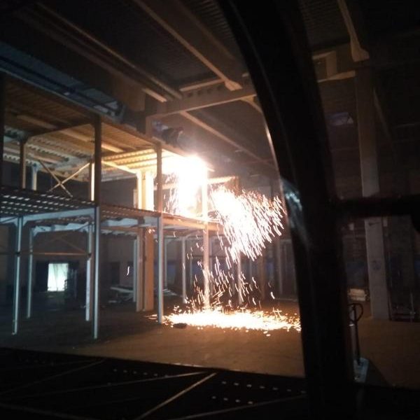 Funken sprühen in einer dunklen, industriellen Umgebung mit Stahlträgern.