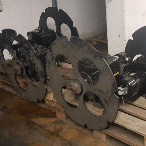 Schwarze Maschinenbauteile mit großen Zahnrädern auf einer Holzpalette.