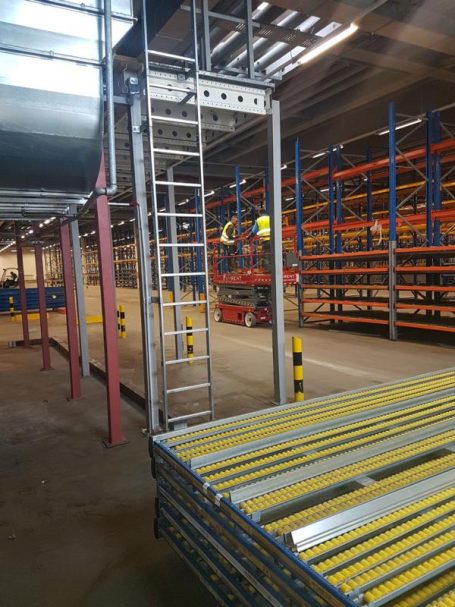 Lagerhalle mit Regalen, Leitern und orangefarbenen Rohren im Hintergrund.