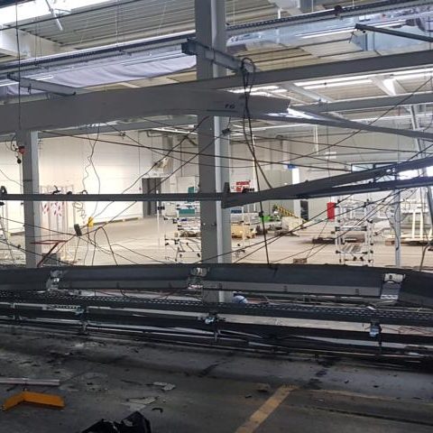 Eine leere Lagerhalle mit beschädigten Regalen und Baugeräten im Hintergrund.