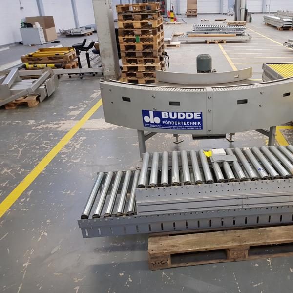 Lagerraum mit Stahlregalen und orangefarbenen Balken. Roter Behälter auf dem Boden.