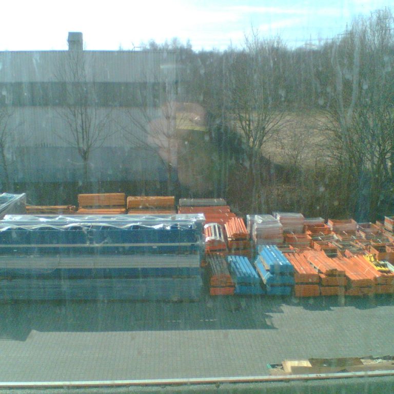 Lagerplatz mit gestapelten Materialien in orange, blau und grau unter klarem Himmel.