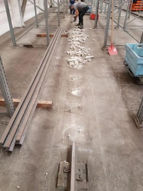 Gleise und Rohre auf dem Boden einer Baustelle, Arbeiter im Hintergrund.