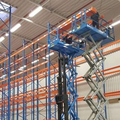 Arbeiter auf einer Hebebühne montieren Regale in einem Lagerhaus.