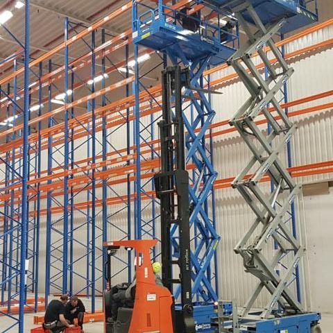 Palette mit Gabelstapler in einem Lager mit einem Scherenlift. Arbeiter sind im Hintergrund aktiv.