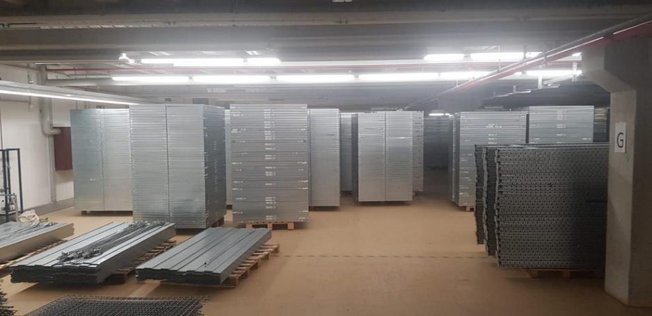 Lagerraum mit gestapelten Metallregalen und leeren Paletten auf dem Boden.