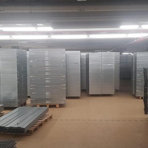 Lagerraum mit gestapelten Metallregalen auf Paletten.