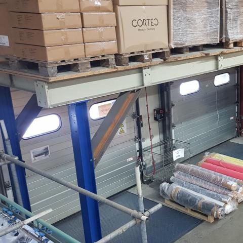 Lagerraum mit gestapelten Kisten und Waren auf Paletten neben einer Ladefläche.