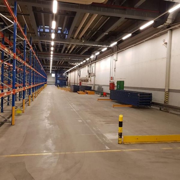 Blick auf einen leeren Lagerraum mit Regalen und gelben Sicherheitsmarkierungen.