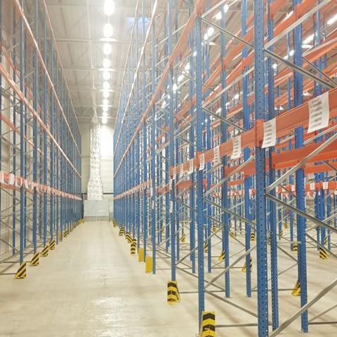 Lagerraum mit hohen Regalen, hell beleuchtet und leer, gelbe Sicherheitsmarkierungen am Boden.