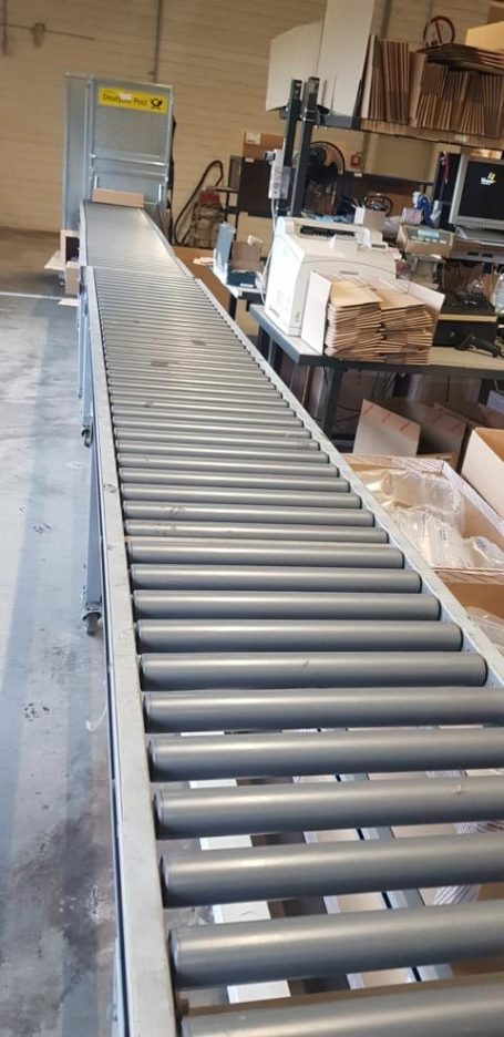 Grau Förderband in einem Lagerraum, mit Holzboxen im Hintergrund.