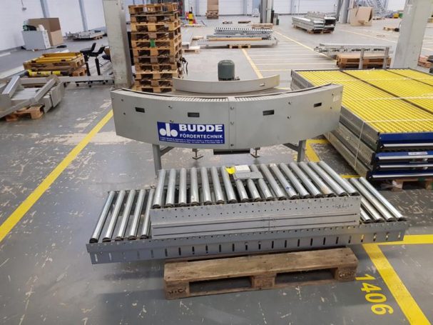 Lagerbereich mit Förderband und Metallregalen auf dem Boden.