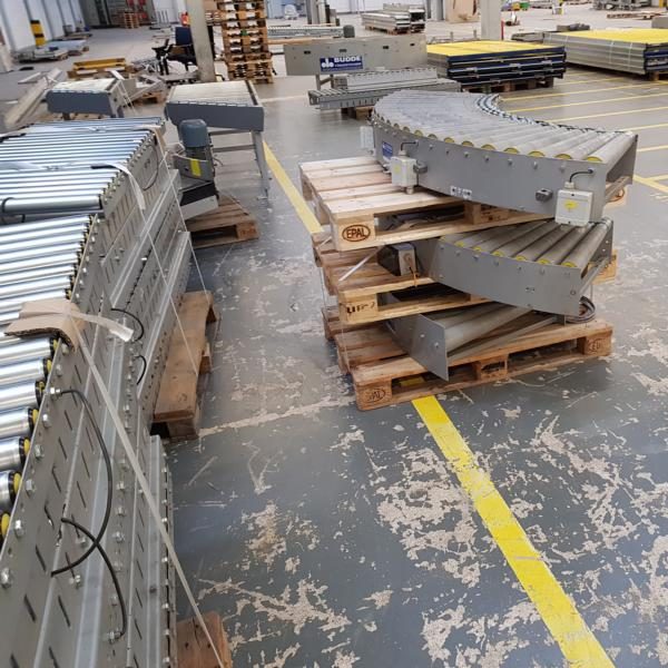 Lagerhalle mit Holzpaletten und gestapelten grauen Bauteilen auf dem Boden.