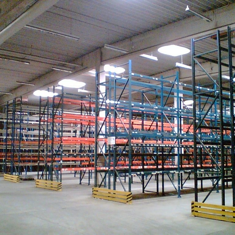 Leere Lagerhalle mit blauen Regalsystemen und orangefarbigen Ablagen.