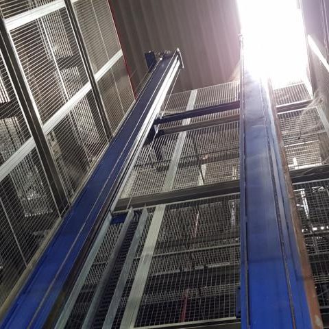 Aufsicht auf einen hohen, blauen Aufzug mit Gitterwänden und hellem Licht oben.