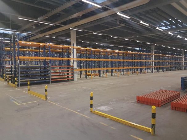 Leerer Lagerraum mit farbigen Regalsystemen und Sicherheitsbarrieren.