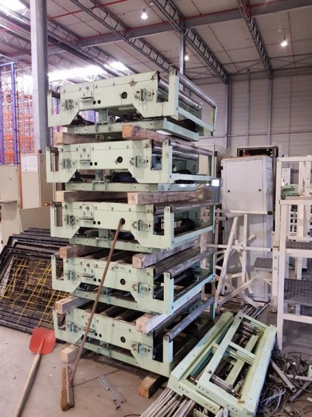 Gestapelte Metallrahmen in einer Lagerhalle, umgeben von Werkzeugen und Geräten.