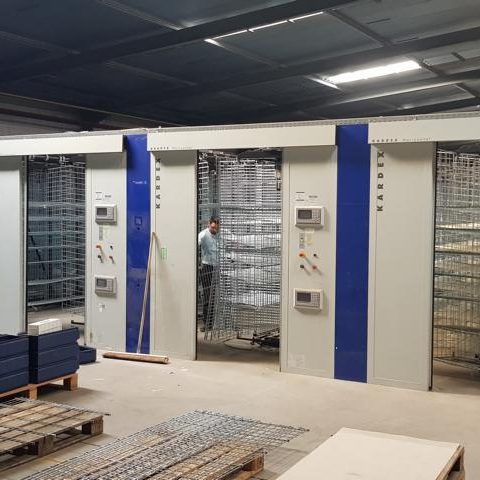 Lagerraum mit Regalsystemen und einem Mitarbeiter zwischen den Regalen.