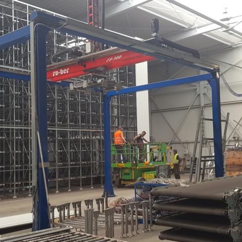 Ein Lagerbereich mit Kränen, Regalen und einem Arbeitskran im Einsatz.