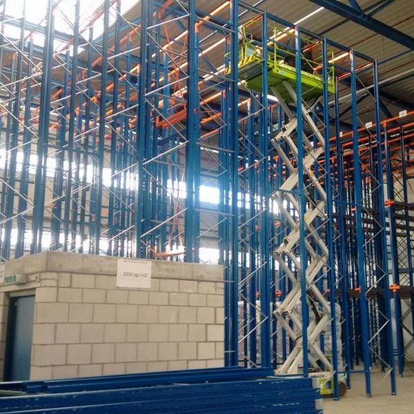 Blick auf ein Hochregallager mit blauen Stahlregalen und einem Hebeaufzug.