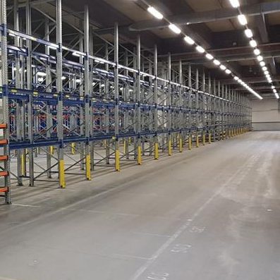 Lagerraum mit hohen Regalen und einem leeren Bodenbereich.