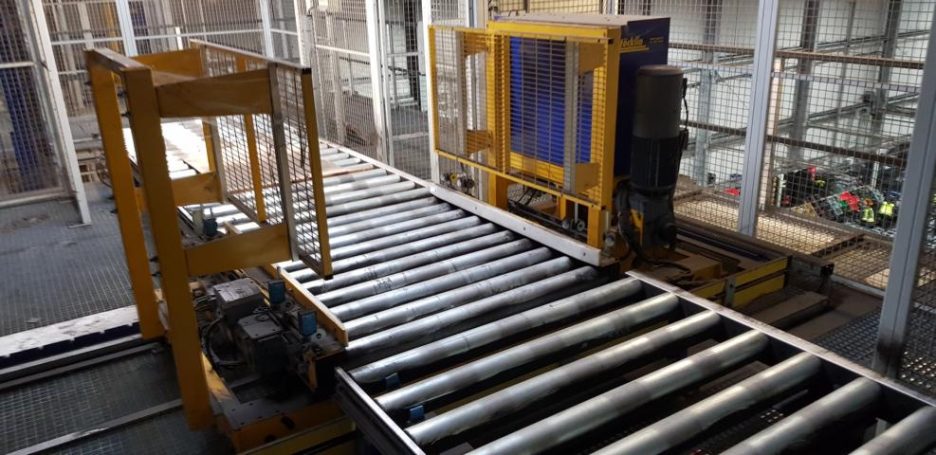 Förderanlage mit Metallrohren auf einer Walze, gelbe Struktur im Hintergrund.