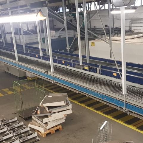 Leere Förderbahn in einer Lagerhalle mit Metallteilen im Vordergrund.