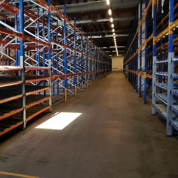 Leerer Lagerraum mit hohen Regalen und Sonnenlicht auf dem Boden.