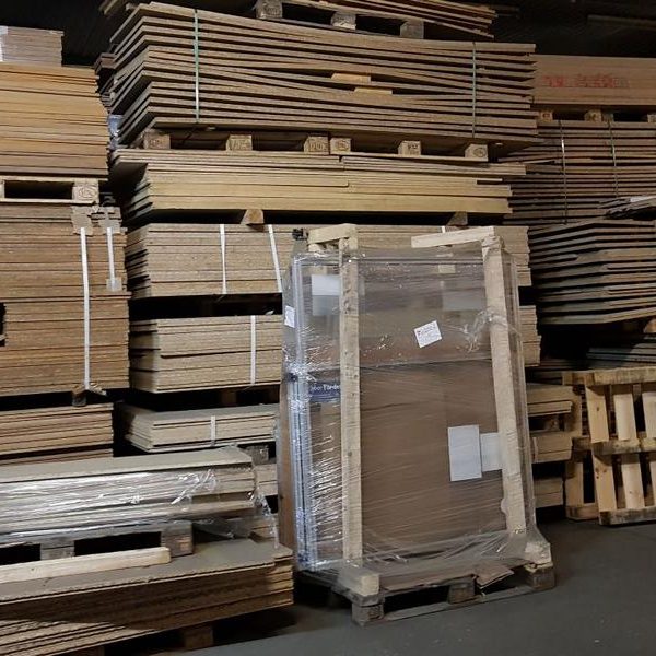 Lager mit gestapelten Holzplatten und Paletten in einer Lagerhalle.