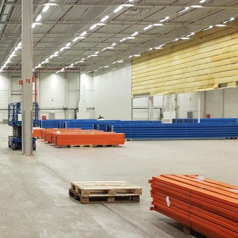 Großer Lagerraum mit orangefarbenen und blauen Stahlträgern auf Paletten.