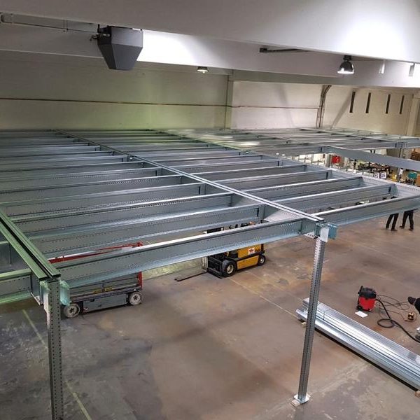 Blick auf ein Stahlgerüst in einer großen, hellen Halle mit Personen im Hintergrund.