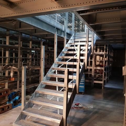 Metallene Treppe in einem Lagerraum mit Regalen im Hintergrund.