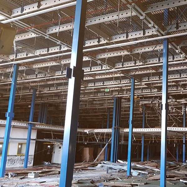 Verlassene Fabrikhalle mit blauen Stahlstützen und unordentlichem Boden.