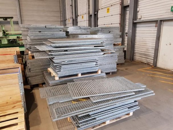 Stapel von verzinkten Metallplatten auf Holzpaletten in einer Lagerhalle.