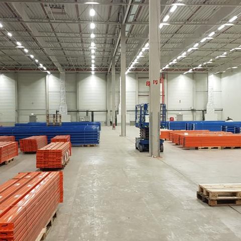 Leere Lagerhalle mit blauen und orangefarbenen Paletten auf dem Boden.