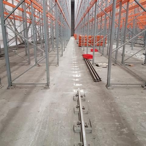 Leerer Lagergang zwischen Regalen mit orangefarbenen Auflagen und grauem Boden.