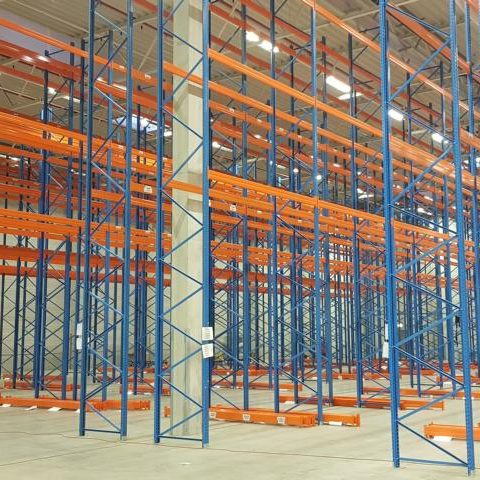 Leere Lagerhalle mit blauen und orangefarbenen Regalsystemen.