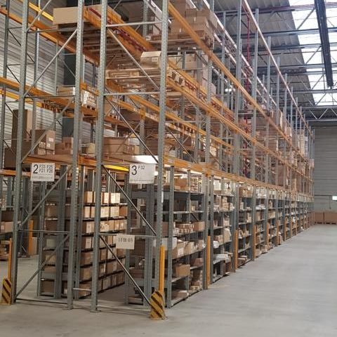 Lagerhalle mit hohen Regalen voller Kartons und einer geräumigen Durchfahrt.