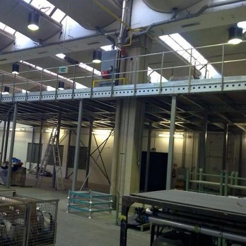 Industrielle Halle mit mehreren Ebenen, Regalen und Arbeitsbereichen.